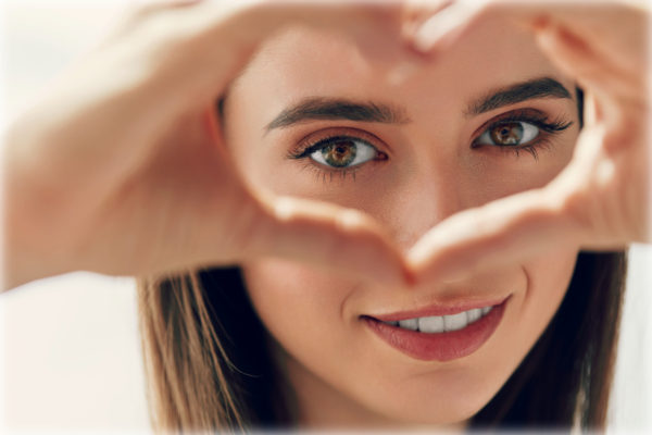 Healthy Eyes And Vision. Portrait Of Beautiful Happy Woman Holding Heart Shaped Hands Near Eyes. Closeup Of Smiling Girl With Healthy Skin Showing Love Sign. Eyecare. 